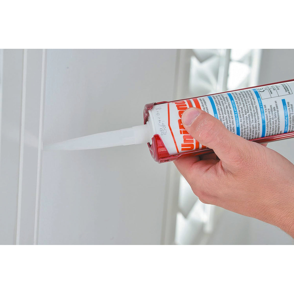 Tajima red heavy-duty sealant caulk gun being used to apply white sealant along a wall joint.